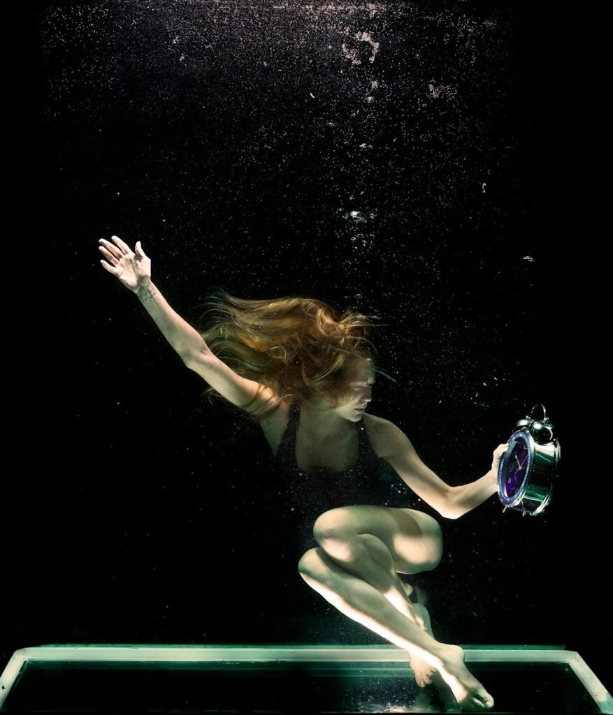 Artistic photo of a woman underwater holding a clock, symbolizing time.